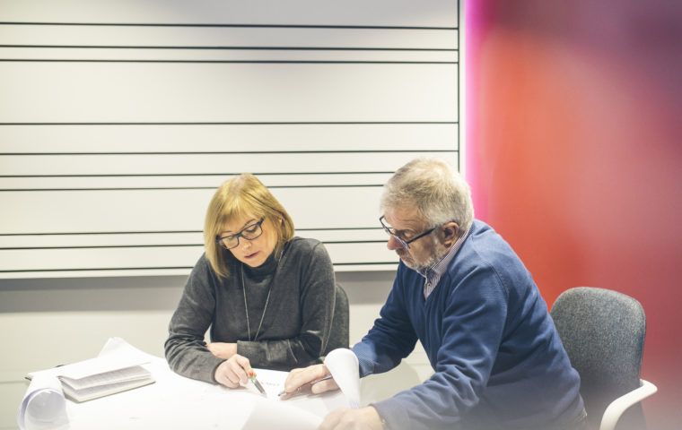 Man and woman sitting at desk pointing at table of work sheets on desk