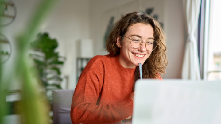 smiling office worker looking at laptop with pen in hand