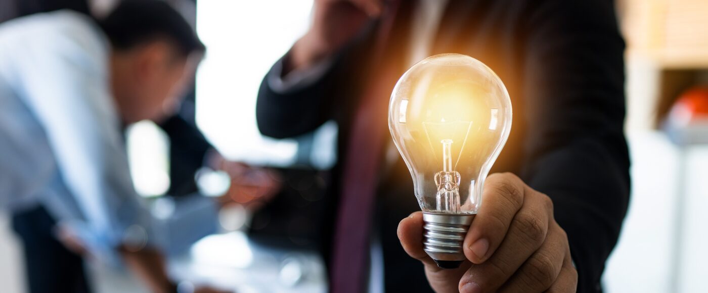 Person holding lightbulb with people working in the background