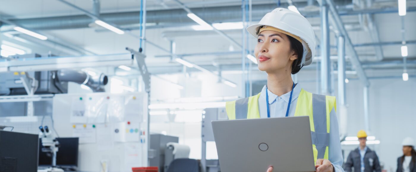 A happy and smiling female engineer in white hard hat with laptop
