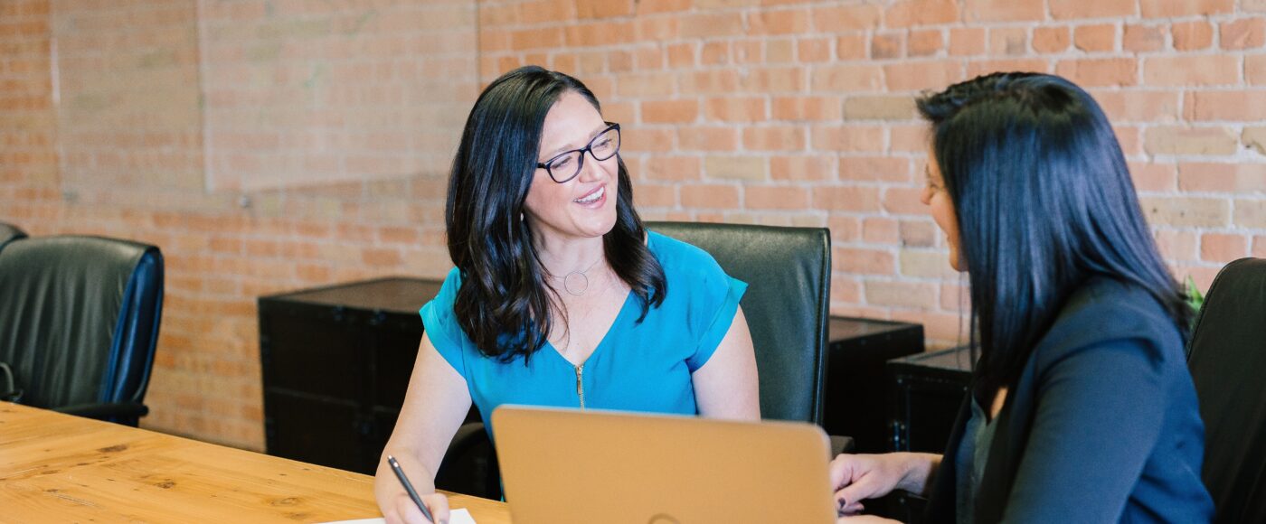 Woman in teal t shirt sitting beside woman in black suit